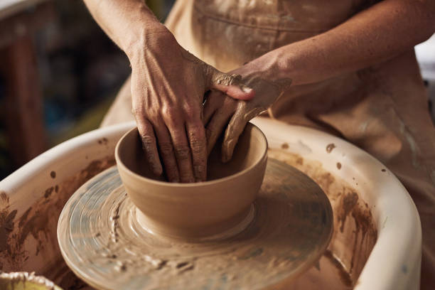 istock Pottery artist, creative or designer touching clay with hands to mold, shape or make handmade ceramic product on potters wheel. Closeup of artistic potter in art studio, workshop or hobby craft store 1413753494