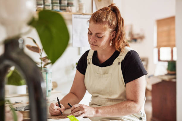 istock Creative business owner writing in a startup shop while taking care of admin duties. Professional artist or craftswoman ordering supplies and customer orders in a workshop for handmade products 1413754937