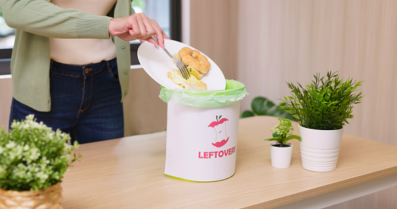close up of asian woman scraping food leftovers or waste into kitchen bucket - Waste separation and environmental friendly at home