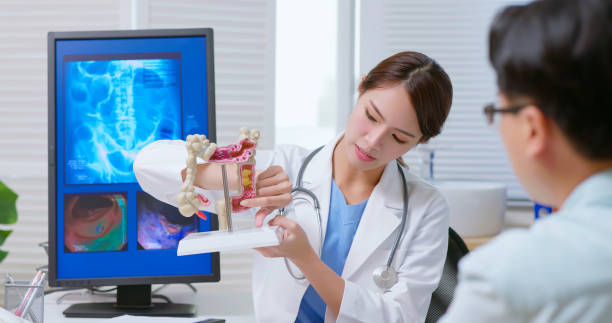 doctor explain colon model attractive young brunette ponytail female asian doctor wear white coat and stethoscope explaining colon model to sick male patient at clinic- an xray film display on computer colonoscopy stock pictures, royalty-free photos & images
