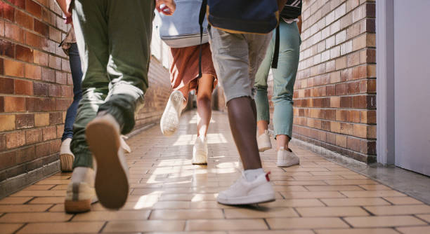 授業に向かう途中の廊下や教育現場で走ったり歩いたりする遅刻した活発な学校の子供たち。休憩中に急いでいる、または遊びに行く若い、小さな学生のグループの低角度の足 - hall way ストックフォトと画像