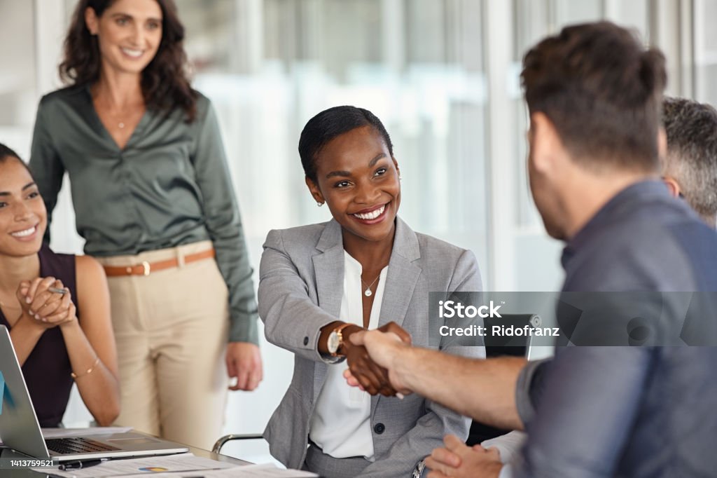 Mature black businesswoman shaking hands with new business partner Happy black businesswoman and businessman shaking hands at meeting. Professional business executive leaders making handshake agreement. Happy business man closing deal at negotiations with african american woman. Business Stock Photo