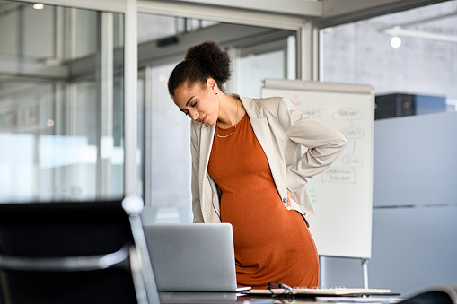 Mujer de negocios embarazada negra que sufre dolor de espalda en la oficina moderna photo