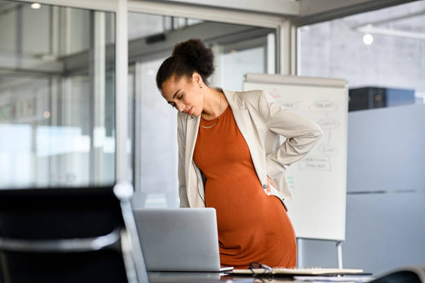 Black pregnant business woman suffering backache at modern office stock photo