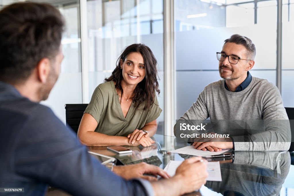 Mature couple meeting financial advisor for investment Smiling mature couple meeting with bank manager for investment. Beautiful mid adult woman with husband listening to businessman during meeting in conference room in modern office. Happy middle aged couple meeting loan advisor to buy a new home. Financial Advisor Stock Photo