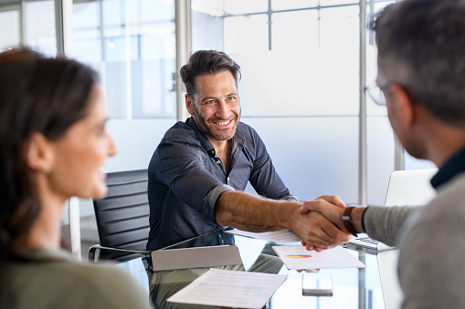 Businessman handshake with couple during meeting to protect their investments. Handshake of a manager with mature couple after agreement for financial investment. Happy financial advisor shaking hands with his client after insurance deal.