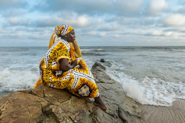 African woman with long dress sitting on stone cliff African woman with long dress sitting on stone cliff after the coast in Accra Ghana West Africa ghana stock pictures, royalty-free photos & images