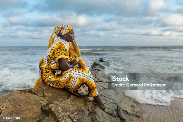 African Woman With Long Dress Sitting On Stone Cliff Stock Photo - Download Image Now
