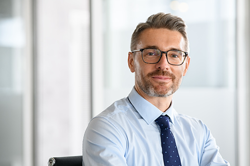 Portrait of successful business man with eyewear in office. Happy and smiling businessman standing in office while looking at camera with copy space. Portrait of handsome mature man in a modern workplace.