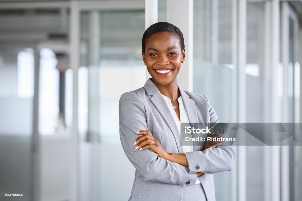 Portrait of successful african american business woman Portrait of mid adult successful black mature woman looking at camera with arms crossed. Smiling african american business woman standing in new office with copy space. Portrait of mature beautiful and confident businesswoman with big smile on her face. Businesswoman Stock Photo