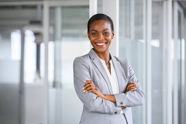 Portrait of successful african american business woman Portrait of mid adult successful black mature woman looking at camera with arms crossed. Smiling african american business woman standing in new office with copy space. Portrait of mature beautiful and confident businesswoman with big smile on her face. businesswear stock pictures, royalty-free photos & images