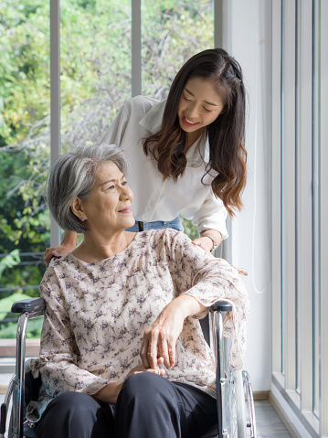 Young asian woman help pushing a wheelchair for grandma in front of corridor with glass wall.