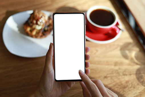 Woman's hand holding a smartphone in a cafe. Smartphone with blank screen for design mockup