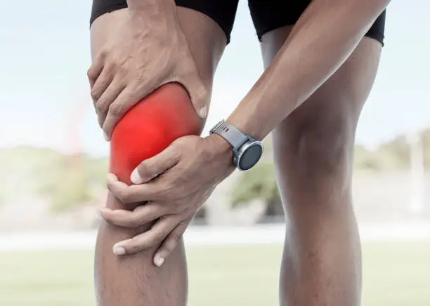 Photo of Closeup of one sportsman holding his sore knee in glowing red. Uncomfortable athlete suffering from a painful leg injury and inflamed muscles during workout. Muscle strain due to overexertion