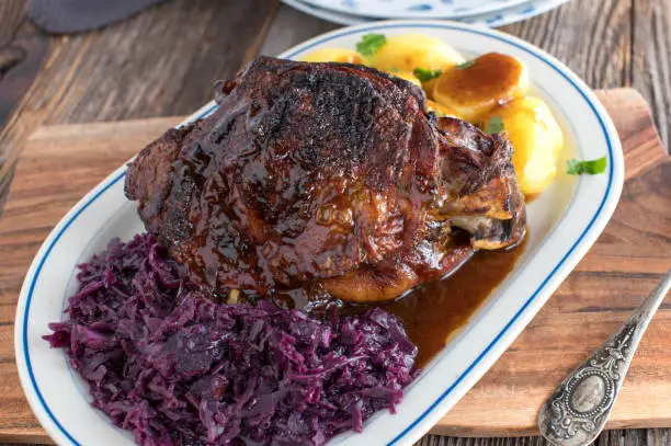Delicious homemade cooked holiday roast with roasted turkey shank, red cabbage, boiled potatoes and brown sauce. Served isolated on wooden table background. Traditional german cuisine.