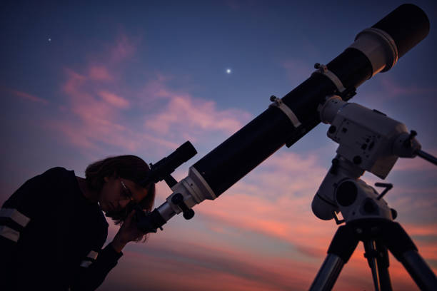 istock Girl with astronomical telescope stargazing under twilight sky. 1413769461