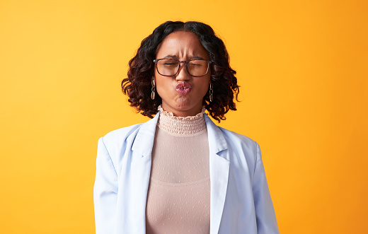Fun, trendy and free black woman showing a kiss and being playful while having fun against a yellow background. Young African American female feeling silly while pulling her face in a pouting gesture