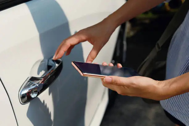 Cropped image of an Asian woman using mobile app device on smartphone to unlock the car doors. Wireless and modern technology concept.