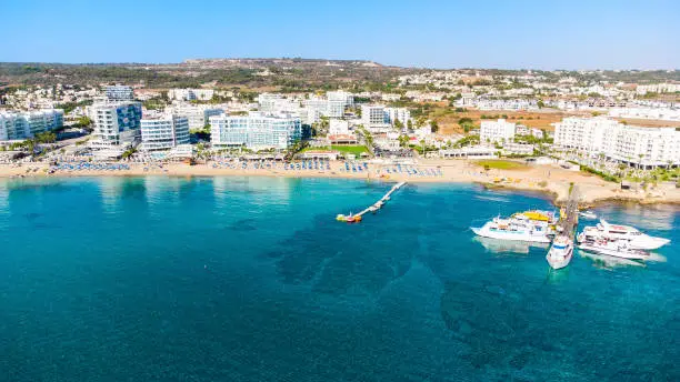 Aerial bird's eye view of Sunrise beach at Fig tree in Protaras, Paralimni, Famagusta, Cyprus. The famous tourist attraction family bay with golden sand, boats, sunbeds, restaurants, water sports, people swimming in sea on summer holidays, from above.
