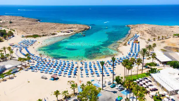 Aerial bird's eye view of Vathia Gonia beach, Ayia Napa, Famagusta, Cyprus. The landmark tourist attraction rocky bay at sunrise with golden sand, sunbeds, sea restaurants in Agia Napa on summer holidays, from above.