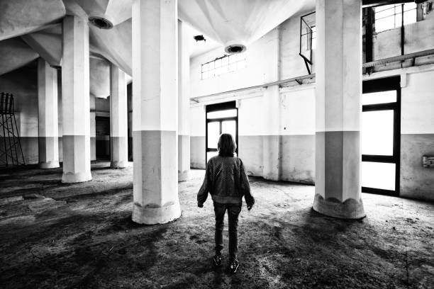 Black & white photo of the woman, serious face expression, dramatic look with the broken windows in the background.