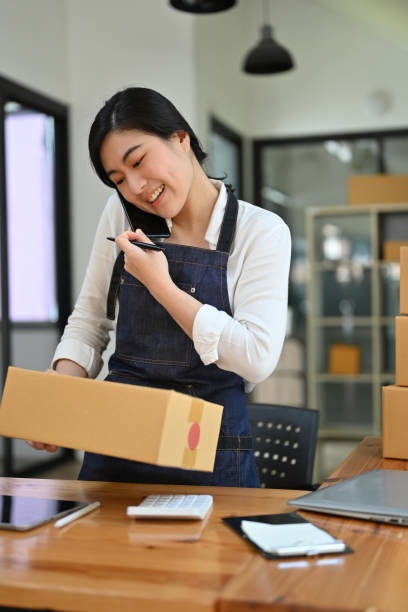 istock Asian female e-commerce business startup talking on the phone while preparing a package. 1413772381