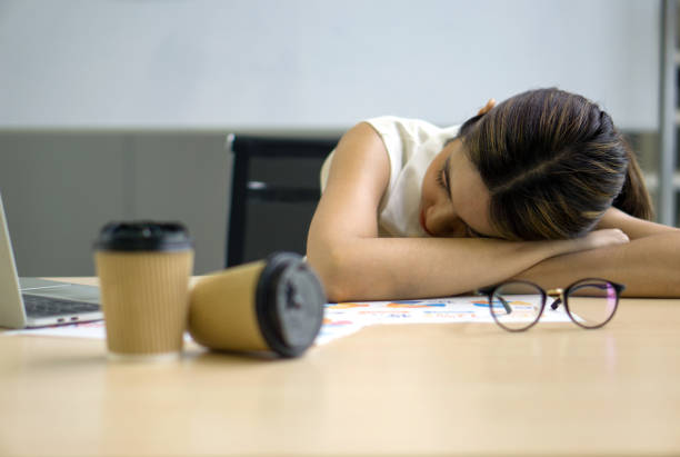 istock Young asian employee take a nap in the office on a table with coffee cup, document, eyeglass and laptop computer. 1413774741