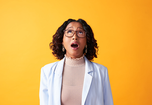 Shocked, surprised and amazed woman looking up at a promotion, message or sale on a yellow copy space background. Stylish, funky and trendy model with mouth open, in awe facial expression and glasses