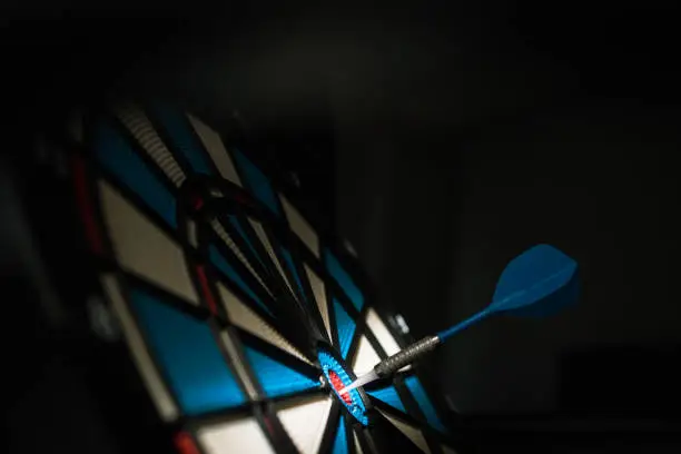 Photo of A dart hitting the center of target with copy space in dramatic light and shadow. Bullseye target or a dart dashboard for financial business planning and targeting with winner goal concept