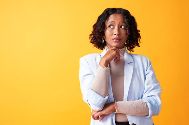 pensar, preguntarse y considerar a una mujer que se ve pensativa y pensativa aislada sobre un fondo amarillo de estudio. mujer africana moderna, elegante y joven preocupada por el futuro con espacio de copia - raised eyebrows women human face thinking fotografías e imágenes de stock