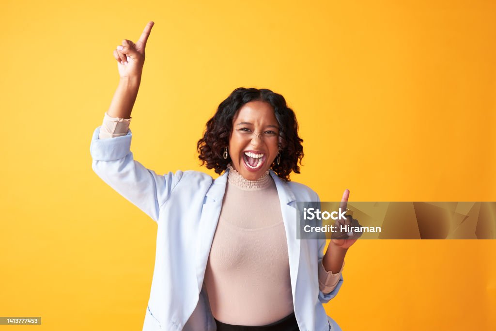 A joyful, cheerful and funny woman dancing against a bright orange background. Portrait of an excited, fun and playful female cheering with fingers pointing up dance. Happy woman doing winner gesture Happiness Stock Photo