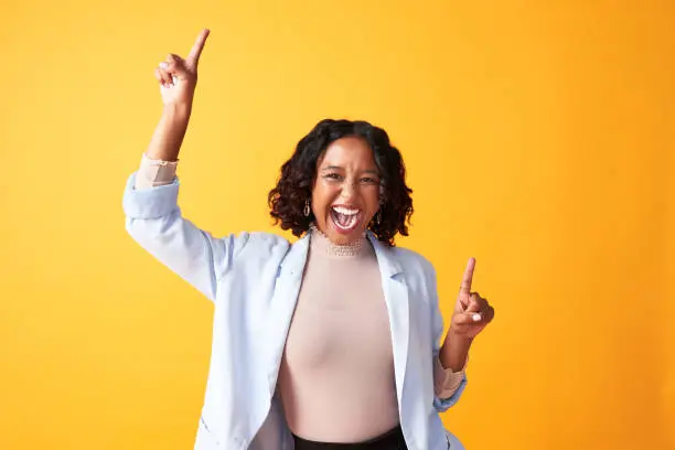 Photo of A joyful, cheerful and funny woman dancing against a bright orange background. Portrait of an excited, fun and playful female cheering with fingers pointing up dance. Happy woman doing winner gesture