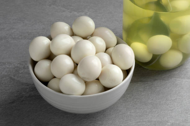 tazón con huevos de codorniz cocidos en conserva de cerca y un frasco de vidrio en el fondo - huevo de codorniz fotografías e imágenes de stock