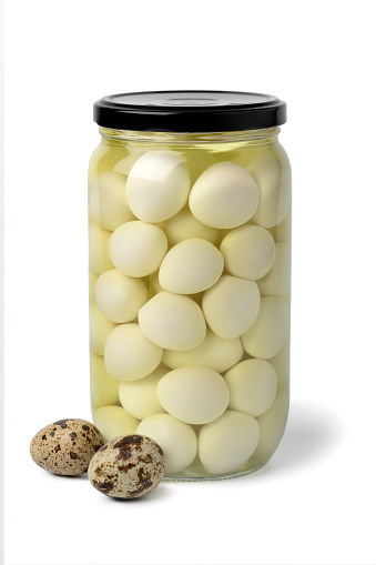 Glass jar with preserved cooked Quail eggs in water close up isolated on white background with fresh raw eggs in front
