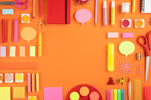 Back to school concept with crayons and school supplies on orange colored background