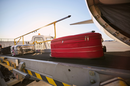 Loading of luggage to airplane. Red suitcase on conveyor belt at airport.
