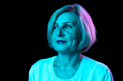 Calm look. Half-length portrait of caucasian senior woman with blond hair posing isolated over dark background in neon light. Concept of natural beauty, ages, fashion, elder generation and ad