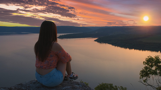The young woman sitting on the mountain top on beautiful river background