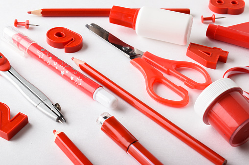 Various stationery of red color in the center on a diagonal on a white background. Back to school. A banner with office elements with space for text. Space for copying. Flat position, top view.