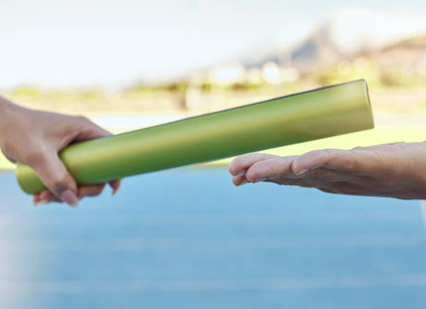 istock Closeup of two athletes passing a baton during a relay race on a running track. Active fit athlete handing the baton over during a relay race to a team member while running in an sport competition 1413785139