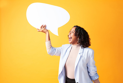 Social media, chatting and conversation expressed by woman holding a speech bubble sign against a yellow background. Happy, excited and cheerful shouting and screaming holding a board with copyspace