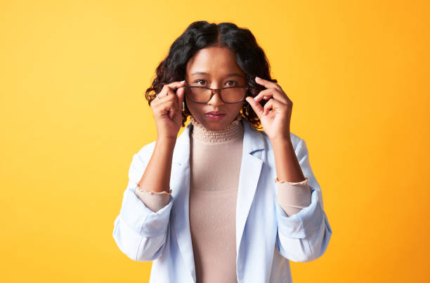 istock Critical boss woman with vision problems wearing glasses against a bright orange background. Portrait of a confident female holding eyewear or looking over spectacles with an elegant style or fashion 1413785507