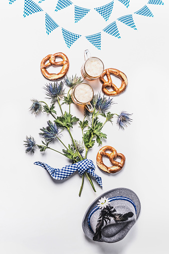Beer Fest composition with traditional Bavarian white blue fabric , decoration, pretzel , cups of draft beer, Bavarian hat and bunch of alpine flowers on white background. Top view. Flat lay