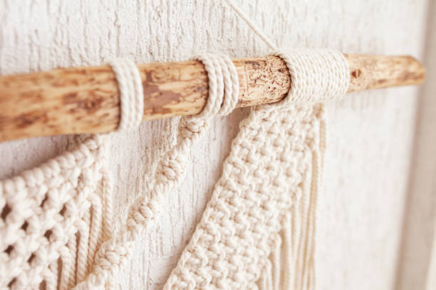 istock Handmade macrame. 100% cotton wall decoration with wooden stick hanging on a white wall.   Macrame braiding and cotton threads.  Female hobby.  ECO friendly modern natural decoration concept 1413794008