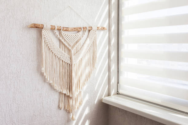 istock Handmade macrame. 100% cotton wall decoration with wooden stick hanging on a white wall.   Macrame braiding and cotton threads.  Female hobby.  ECO friendly modern natural decoration concept 1413794020