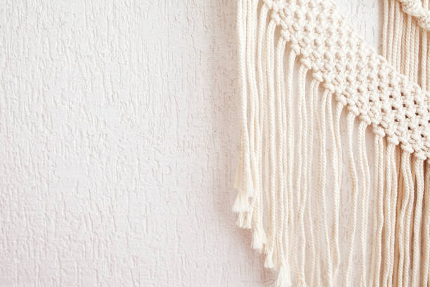 istock Handmade macrame. 100% cotton wall decoration with wooden stick hanging on a white wall.   Macrame braiding and cotton threads.  Female hobby.  ECO friendly modern natural decoration concept 1413794021