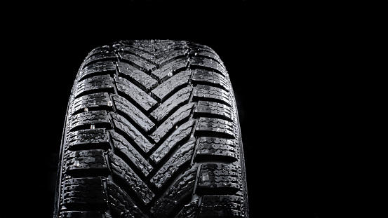 Close-up of wet vehicle tyre against black background.