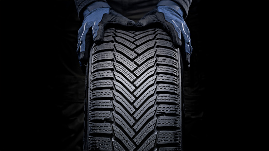 Close-up of man's hands pushing vehicle tyre against black background.