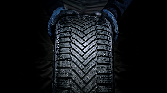 Close-up of man's hands pushing wet vehicle tyre against black background.
