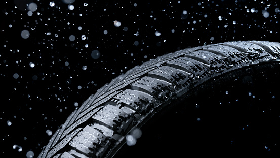 Close-up of water splashing on vehicle tyre against black background.